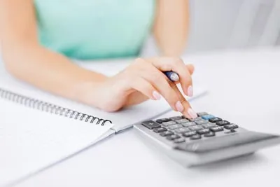 woman using a calculator while writing in a notebook